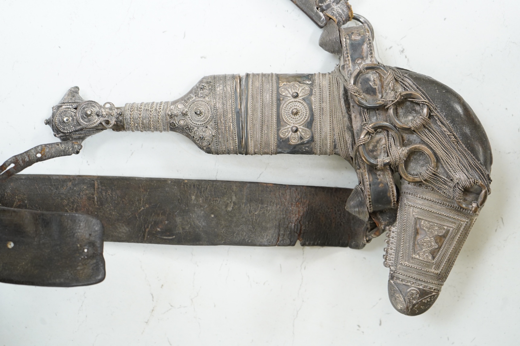 A late 19th century Arab silver mounted dagger jambya with silver filigree mounts to hilt and sheath, in its leather covered scabbard with parts of the original belt